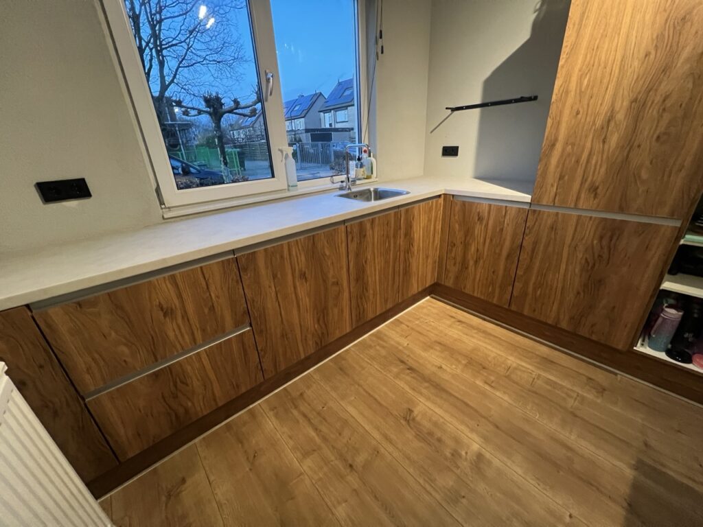 Keuken gewrapt in warme houtlook met zwart kookeiland en betonlook aanrechtblad NH54